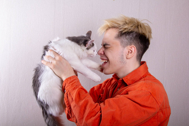 Nastolatek trzyma kota w ramionach, który sięga po twarz łapami. Koncepcja: gra człowieka i zwierzęcia, przywiązanie do zwierząt. - Zdjęcie, obraz