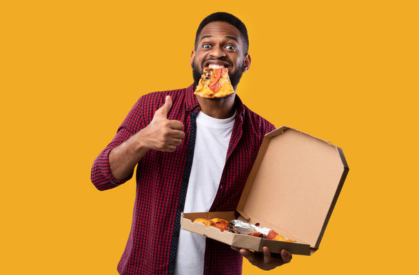 口の中でピザと黒男ジェスチャー親指アップ,黄色の背景 - 写真・画像