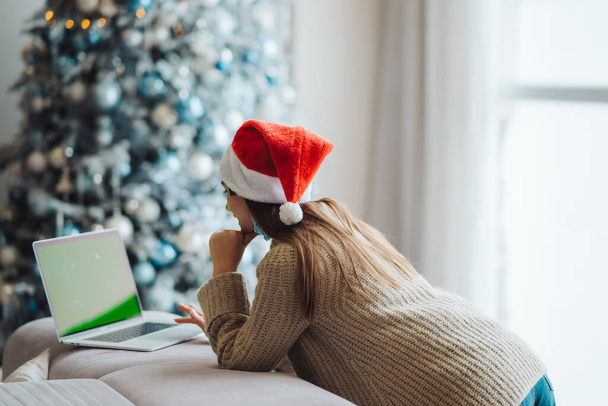 Feminino vestindo chapéu de Papai Noel enquanto fala com amigo on-line no laptop - Foto, Imagem