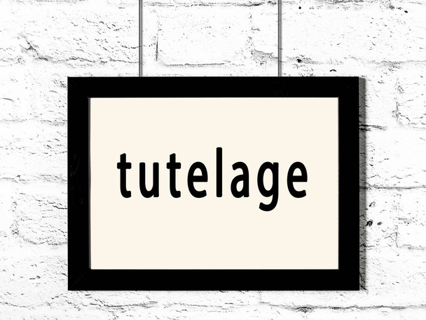 Černý dřevěný rám s nápisem tutelage visí na bílé cihlové zdi  - Fotografie, Obrázek