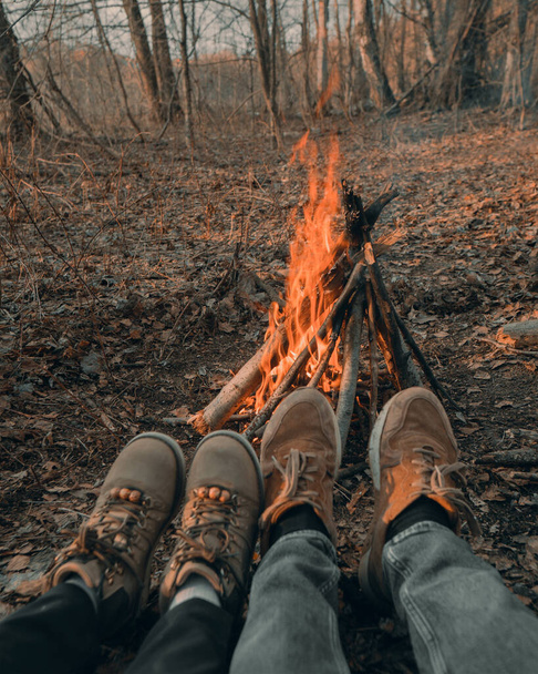 two pairs of legs in sneakers admire the fire in the forest - Фото, изображение