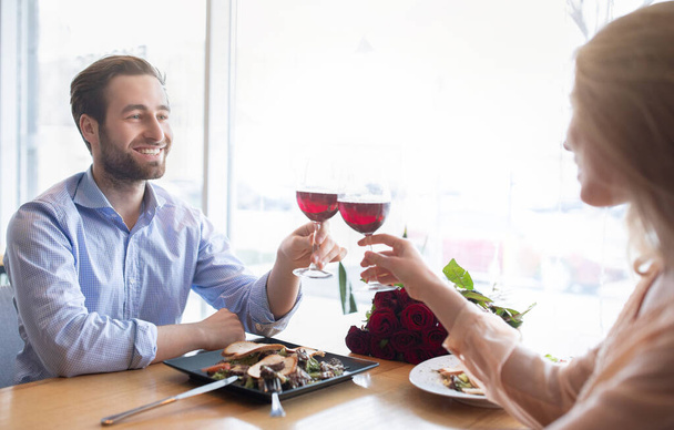 Couple millénaire affectueux célébrant l'anniversaire ensemble, boire du vin, faire du pain grillé dans un café confortable - Photo, image