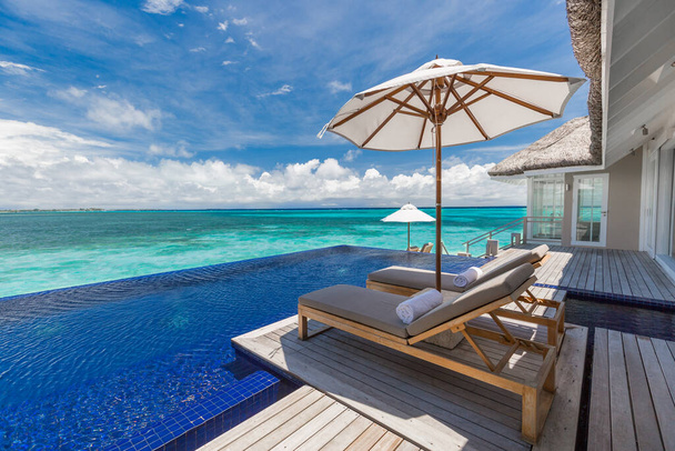 Luxury resort exterior poolside and cloudy blue sky. Luxurious tropical beach landscape, deck chairs and loungers and water reflection. Infinity swimming pool and endless seascape, exotic destination, summer vacation, holiday travel concept.  - Photo, Image