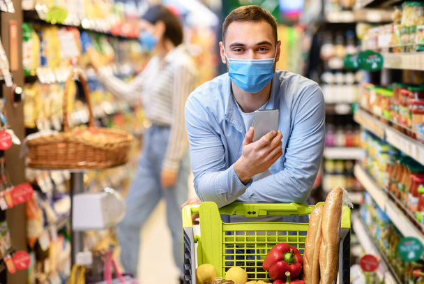 Парень в маске со смартфоном в гипермаркете - Фото, изображение