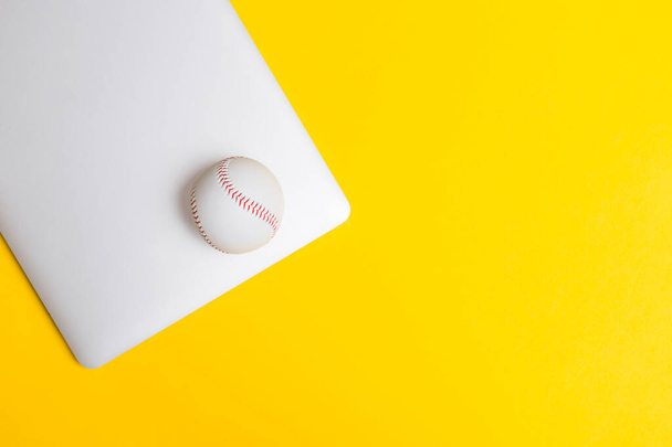 бейсбольный мяч и серый ноутбук на желтом фоне. онлайн тренировки концепции. вид сверху, место для текста - Фото, изображение