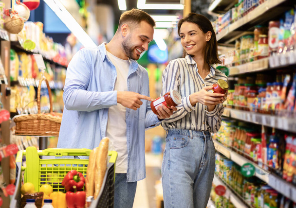Happy millennial couple with the cart shopping in supermarket - Фото, изображение