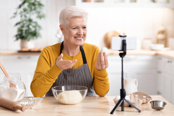 Ηλικιωμένη γυναίκα blogger τροφίμων καταγραφή μαγείρεμα της από την κουζίνα - Φωτογραφία, εικόνα