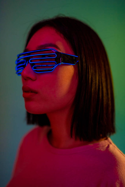 jonge vrouw dragen futuristische led bril geïsoleerd op groene achtergrond clubbing stille disco dragen neon bril - Foto, afbeelding