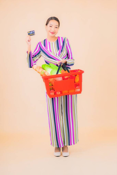 Portrait beautiful young asian woman with grocery basket from supermarket on color isolated background - Foto, Imagem