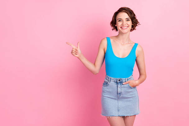Photo of lovely pretty confident young lady directing finger empty space shiny smiling make perfect proposition wear denim mini skirt blue tank-top isolated pink color background - Fotoğraf, Görsel