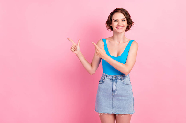 Photo of cute pretty young woman beaming toothy smiling directing fingers empty space propose interesting curious option wear denim mini skirt blue tank-top isolated pink color background - Fotografie, Obrázek