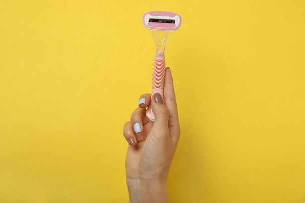 Female hand hold razor on yellow background, space for text - 写真・画像