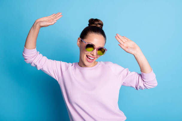 Photo of positive cheerful excited girl enjoy disco discotheque dancing raise hands wear pullover specs eyeglasses isolated over blue color background - Photo, Image