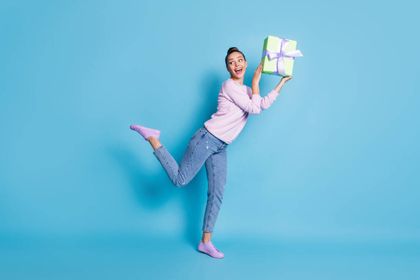 Full length photo of excited enthusiastic girl hold gift box enjoy rejoice anniversary celebration wear good look clothes sneakers isolated over blue color background - Φωτογραφία, εικόνα