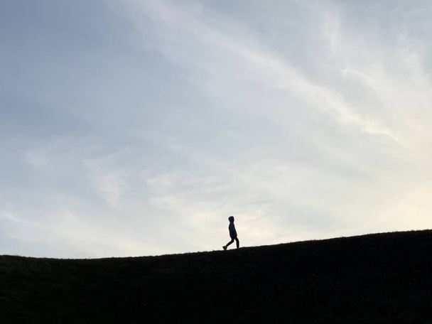 Silhouette of a man on top of a mountain. Man is not a background of earth and sky. Silhouettes of people in the distance on the hill. - Photo, Image