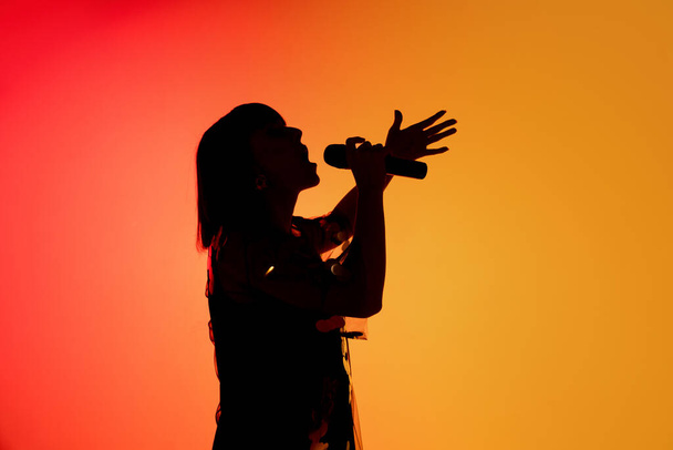 Silhouette einer jungen kaukasischen Sängerin isoliert auf orangefarbenem Studiohintergrund im Neonlicht - Foto, Bild
