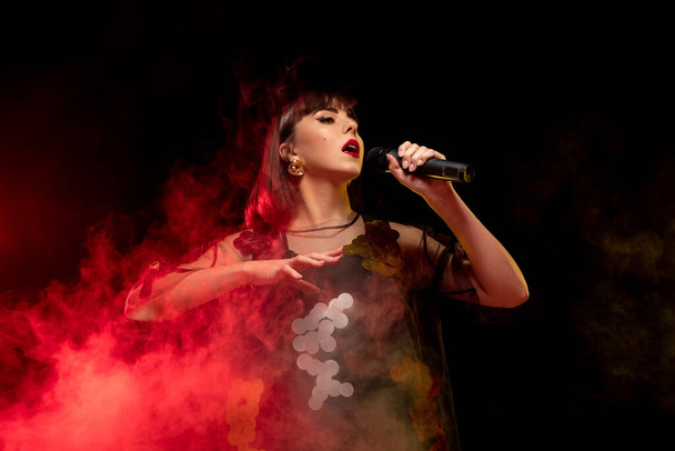 Caucasian female singer portrait isolated on dark studio background in neon light - Zdjęcie, obraz