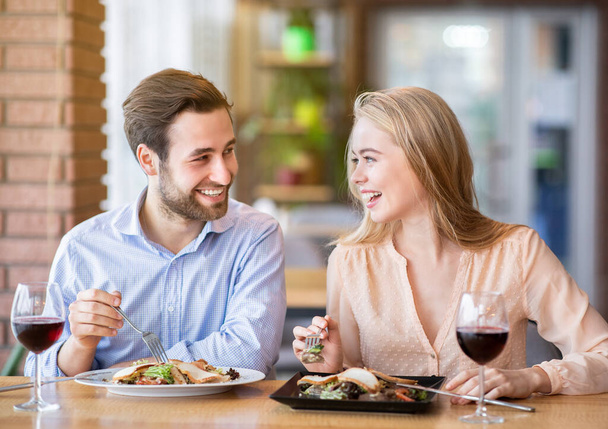 Encantadora dama con su novio comiendo ensalada y bebiendo vino, celebrando aniversario juntos en la cafetería urbana - Foto, imagen
