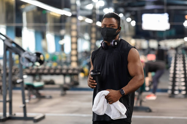 Culturista negro en mascarilla con agua, toalla en el gimnasio - Foto, imagen