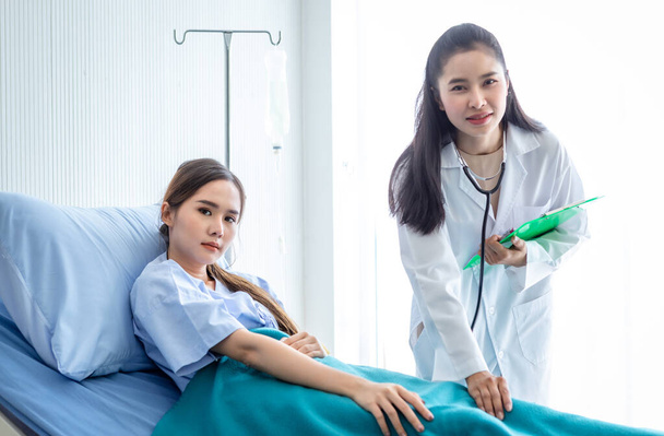 Asiática mujer médico mantenga la pierna para curar la enfermedad a la joven paciente en la cama con síntoma en el fondo del hospital, atención médica, concepto de medicina - Foto, imagen