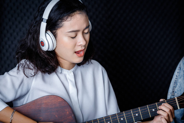 Happy cheerful pretty smiling of portrait a young Asian woman vocalist Wearing Headphones with a Guitar recording a song front of microphone in a professional studio - Foto, immagini