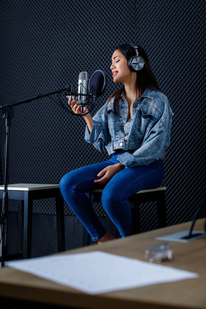 Happy cheerful pretty smiling of portrait of young Asian woman look at the smartphone vocalist Wearing Headphones recording a song front of microphone in a professional studio - Foto, immagini