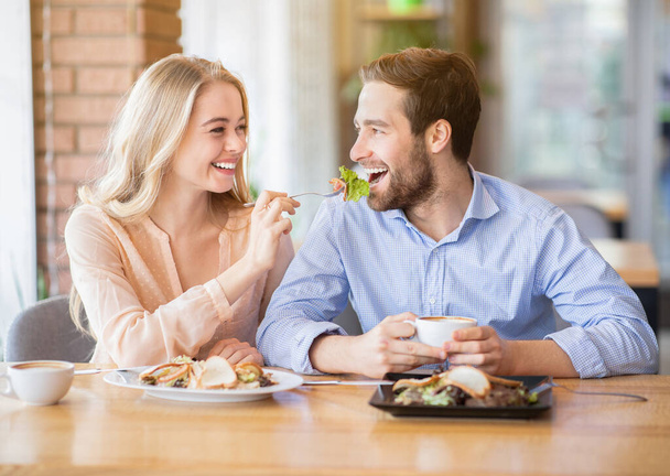 Lovely young woman feeding her boyfriend with fresh salad at coffee shop - Photo, Image