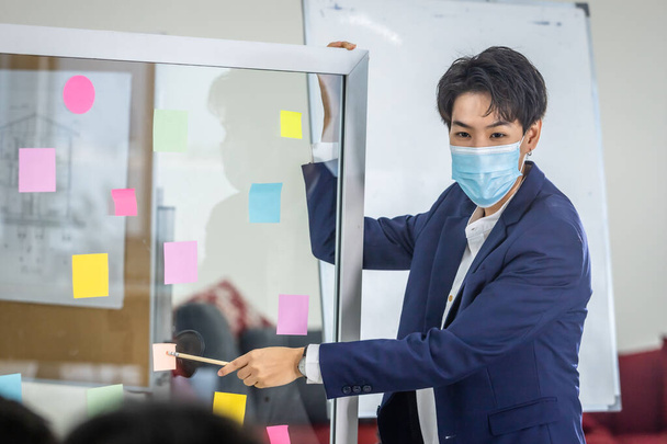 asian Business tomboy lesbian wearing protective mask presenting use post it notes to share idea.Brainstorming concept.Sticky note on glass wall in the meeting room at office,Concept of COVID-19 - Fotó, kép