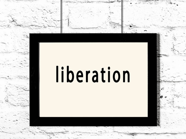 Black wooden frame with inscription liberation hanging on white brick wall  - Photo, Image