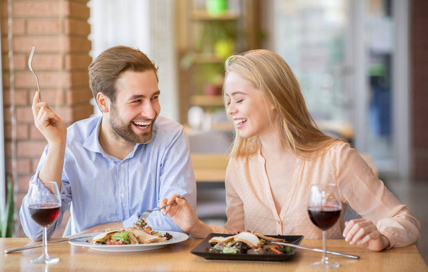 Счастливая молодая пара обедает вместе в кафе, разговаривает и смеется во время еды - Фото, изображение