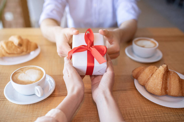 Jeune couple avec cadeau au café, déjeuner ensemble, fête anniversaire, gros plan des mains - Photo, image