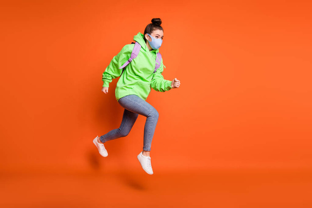 Photo portrait full body view of young girl jumping up running wearing blue fabric face mask isolated on vivid orange colored background - Fotografie, Obrázek