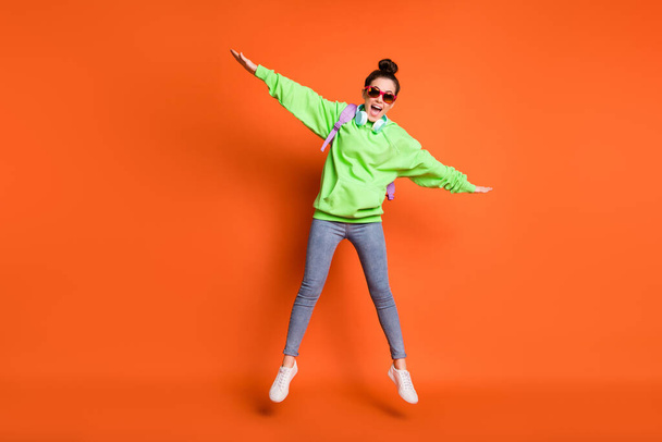 Photo portrait full body view of excited schoolgirl jumping up making wings with hands isolated on vivid orange colored background - Фото, зображення