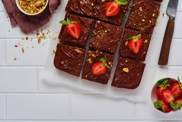 Chocolate squares with pistachio nuts and strawberries on white paper on a light background, top view, horizontal composition. Flat food. - Foto, Bild