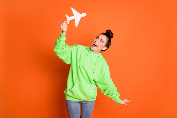 Photo of childish lady dressed green sweatshirt playing white paper plane isolated bright orange color background - Zdjęcie, obraz