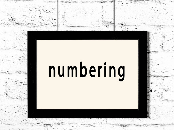 Czarna drewniana rama z napisem numeracja wisząca na białej ceglanej ścianie  - Zdjęcie, obraz