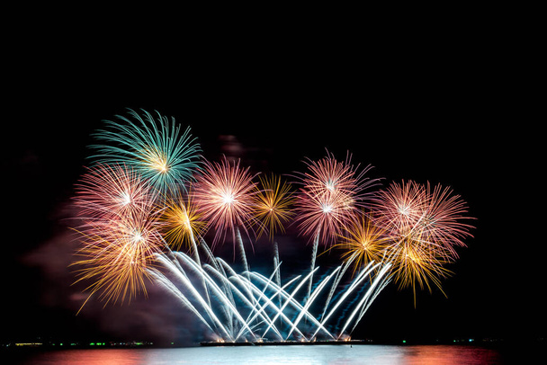 Το χρώμα και η ομορφιά των πυροτεχνημάτων που στήνονται στη θάλασσα, στον μαύρο ουρανό τη νύχτα, για τον εορτασμό του εορτασμού των εορτών, στους ανθρώπους και την ιδέα του Ευτυχισμένου Νέου Έτους. - Φωτογραφία, εικόνα