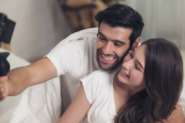 Adorável casal caucasiano deitado na cama e sorrir ao fazer uma selfie usando um phon móvel - Foto, Imagem