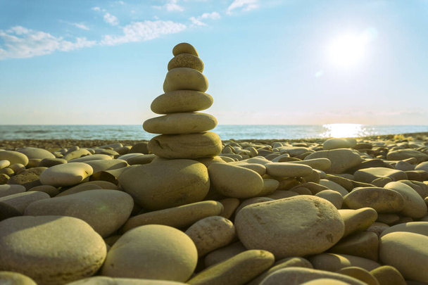 Las piedras se apilan verticalmente en la orilla del mar, la playa rocosa, el cielo azul y el sol cegador. - Foto, Imagen