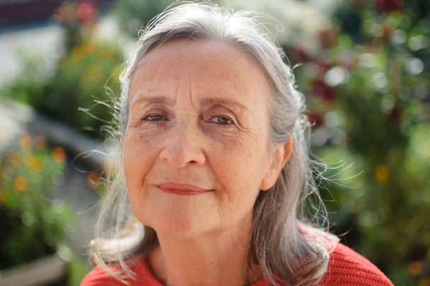 Portret van een volwassen vrouw met grijs haar tijd doorbrengen buiten tijdens zonnige dag, gelukkig pensioen - Foto, afbeelding