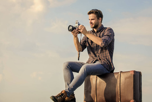 Photojournalist concept. Travel with luggage. Travel blogger. Shooting vlog. Vacation time. Travel blog. Man sit on suitcase. Handsome guy traveler retro camera. Guy outdoors with vintage suitcase - 写真・画像