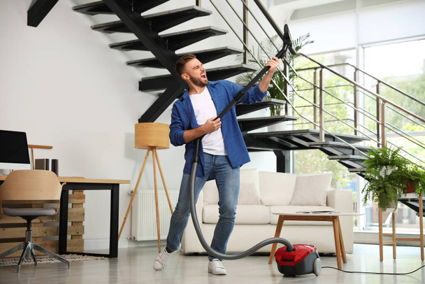 Young man having fun while vacuuming in living room - Fotó, kép