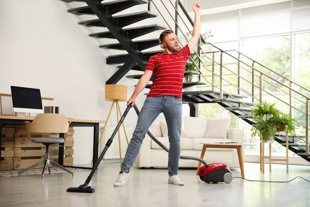 Young man having fun while vacuuming in living room - Foto, imagen