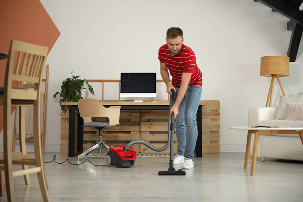 Young man using vacuum cleaner at home - Foto, afbeelding