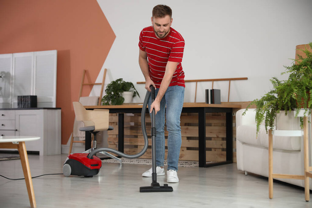 Young man using vacuum cleaner at home - Fotó, kép