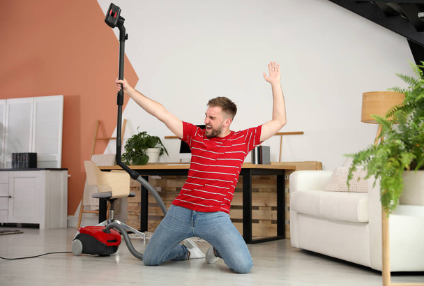 Young man having fun while vacuuming at home - Foto, Imagem