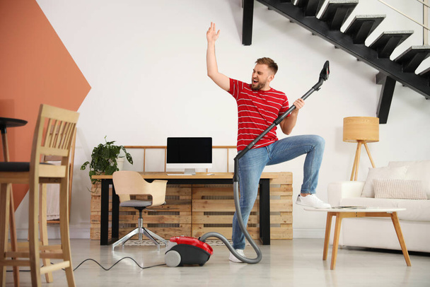 Young man having fun while vacuuming at home - 写真・画像