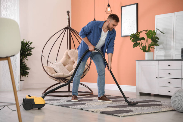 Young man using vacuum cleaner at home - Foto, Imagem