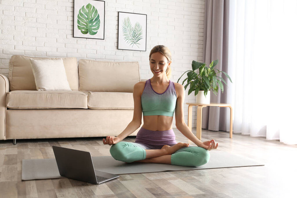 Woman having online video class via laptop at home. Distance yoga course during coronavirus pandemic - Foto, Imagen