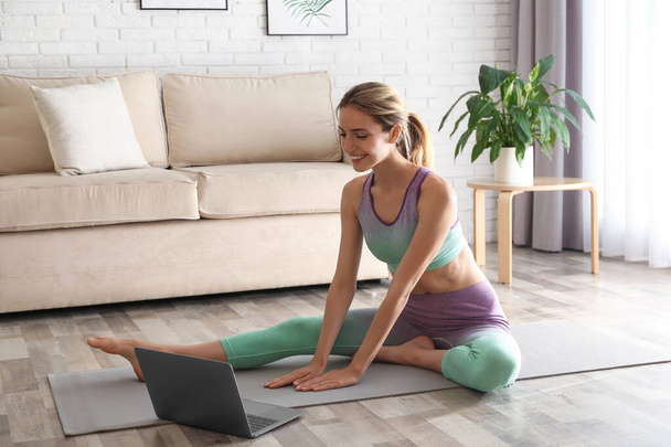 Woman having online video class via laptop at home. Distance yoga course during coronavirus pandemic - Foto, Bild